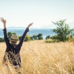 woman's back in tall grass field with arms up