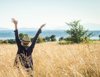woman's back in tall grass field with arms up