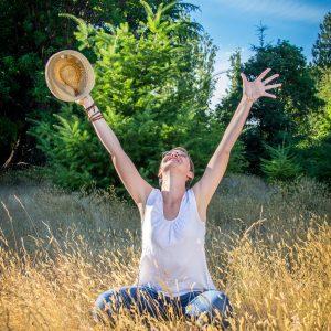 relationships-square woman sitting in tall grass looking up with arms up smiling