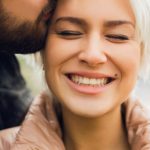 woman smiling while being kissed on the forehead by a man